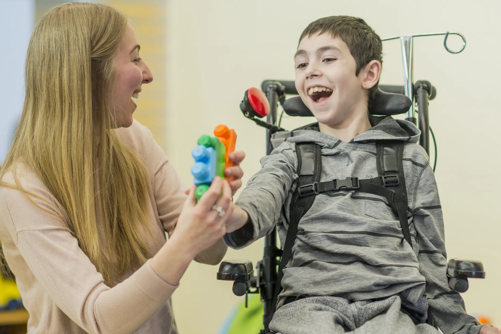 Adult assisting a child in a wheelchair with a colourful toy during a therapy or play session