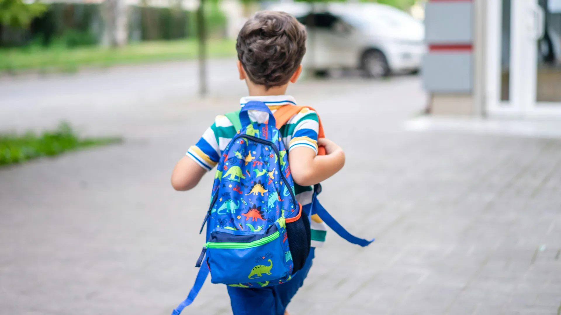 Child walking with a dinosaur-print backpack