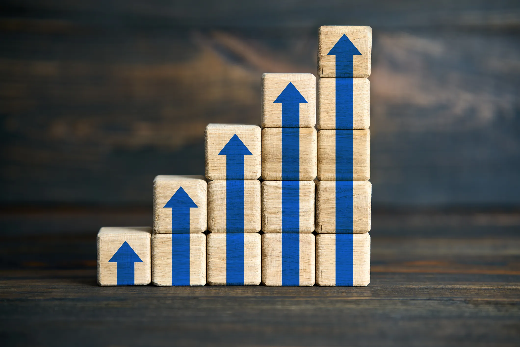 Stacked wooden blocks with blue upward arrows showing growth