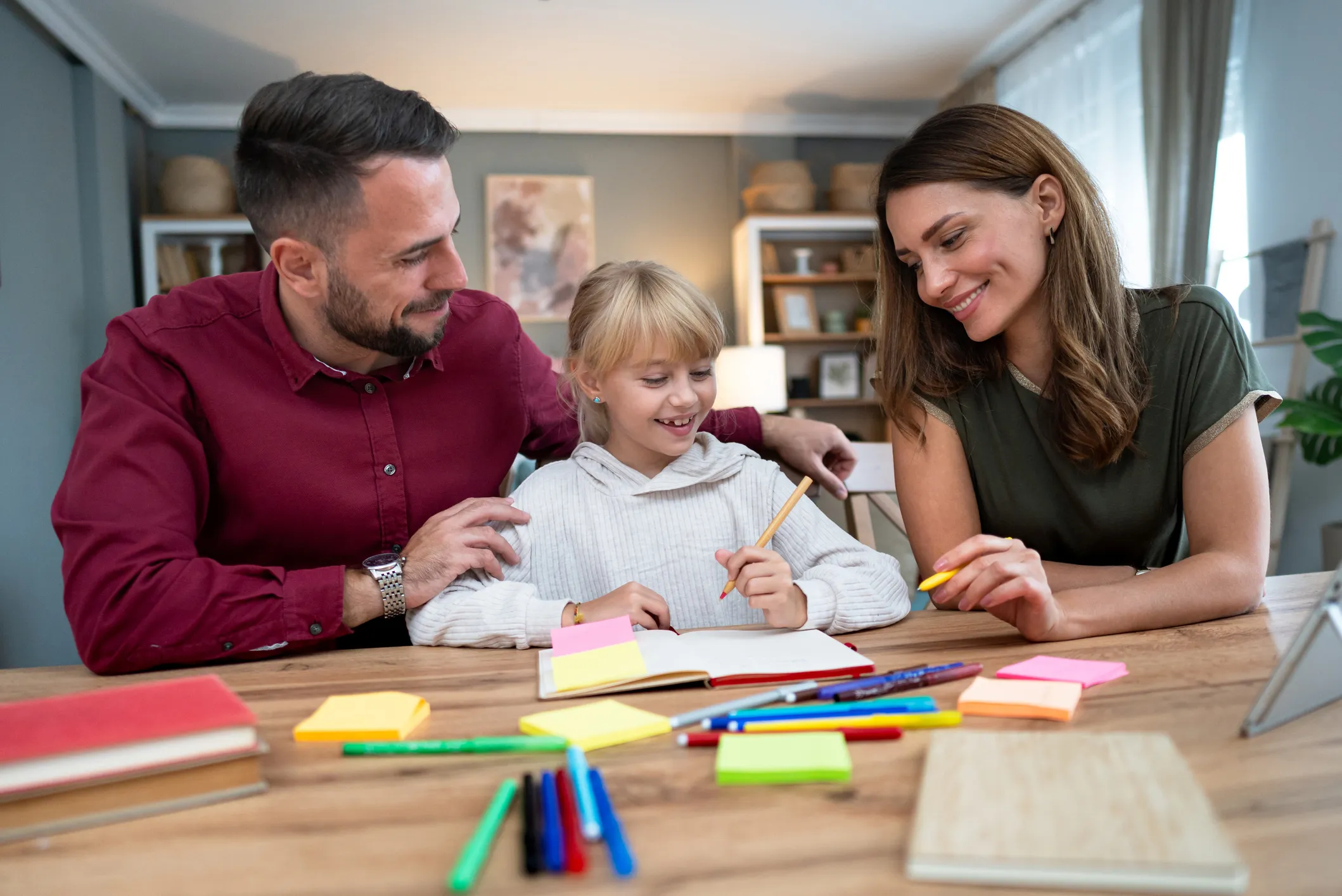 Two adults helping a child with homework at a table covered in stationery