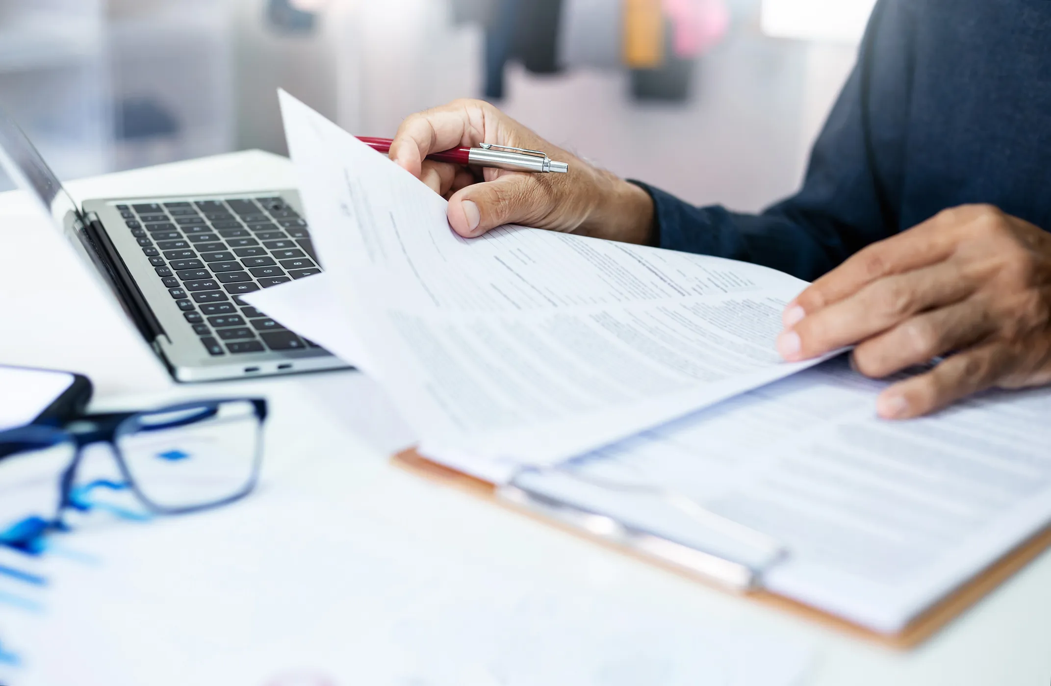 Person reviewing documents while working on a laptop