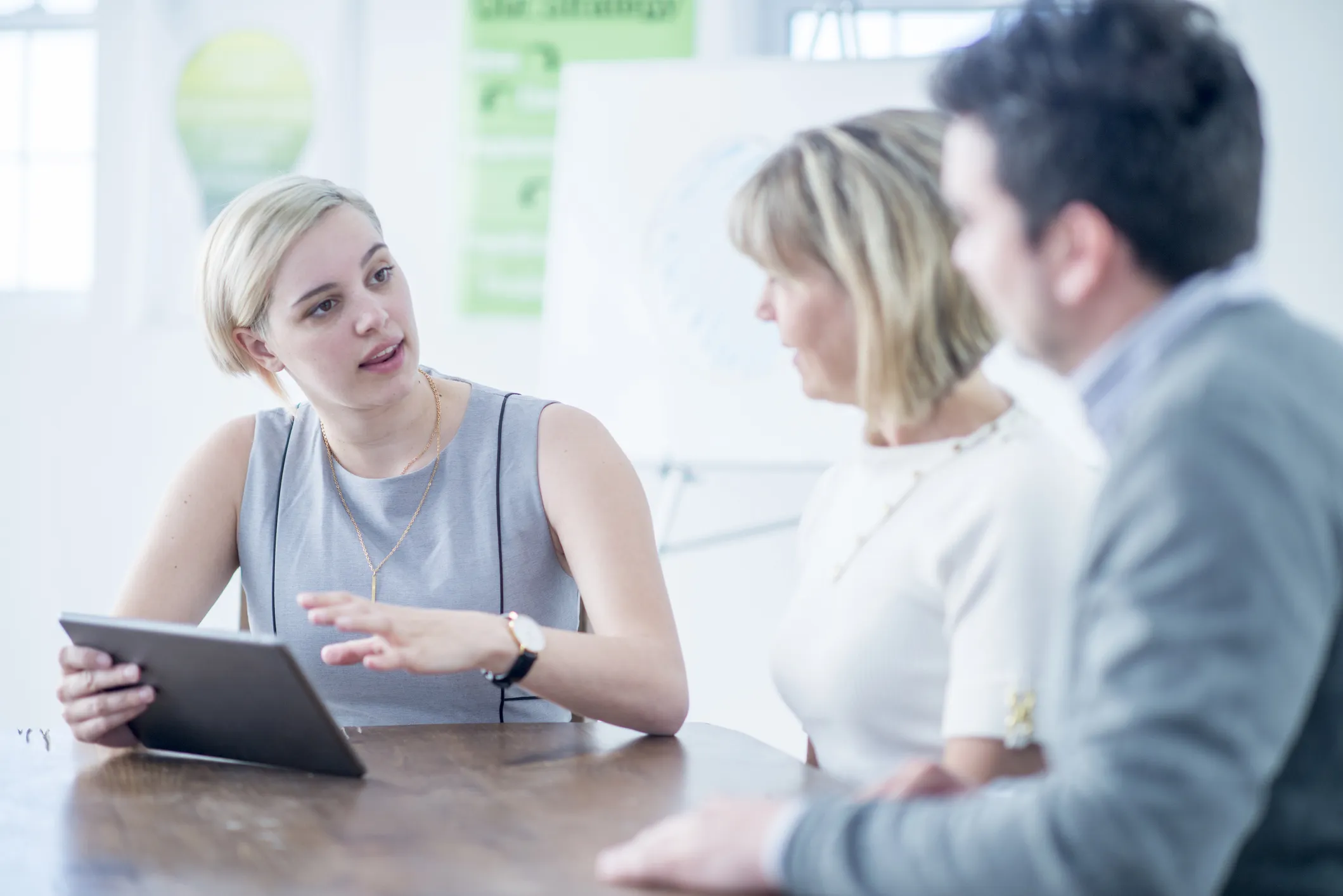 Three people in a meeting, one holding a tablet and speaking to the others