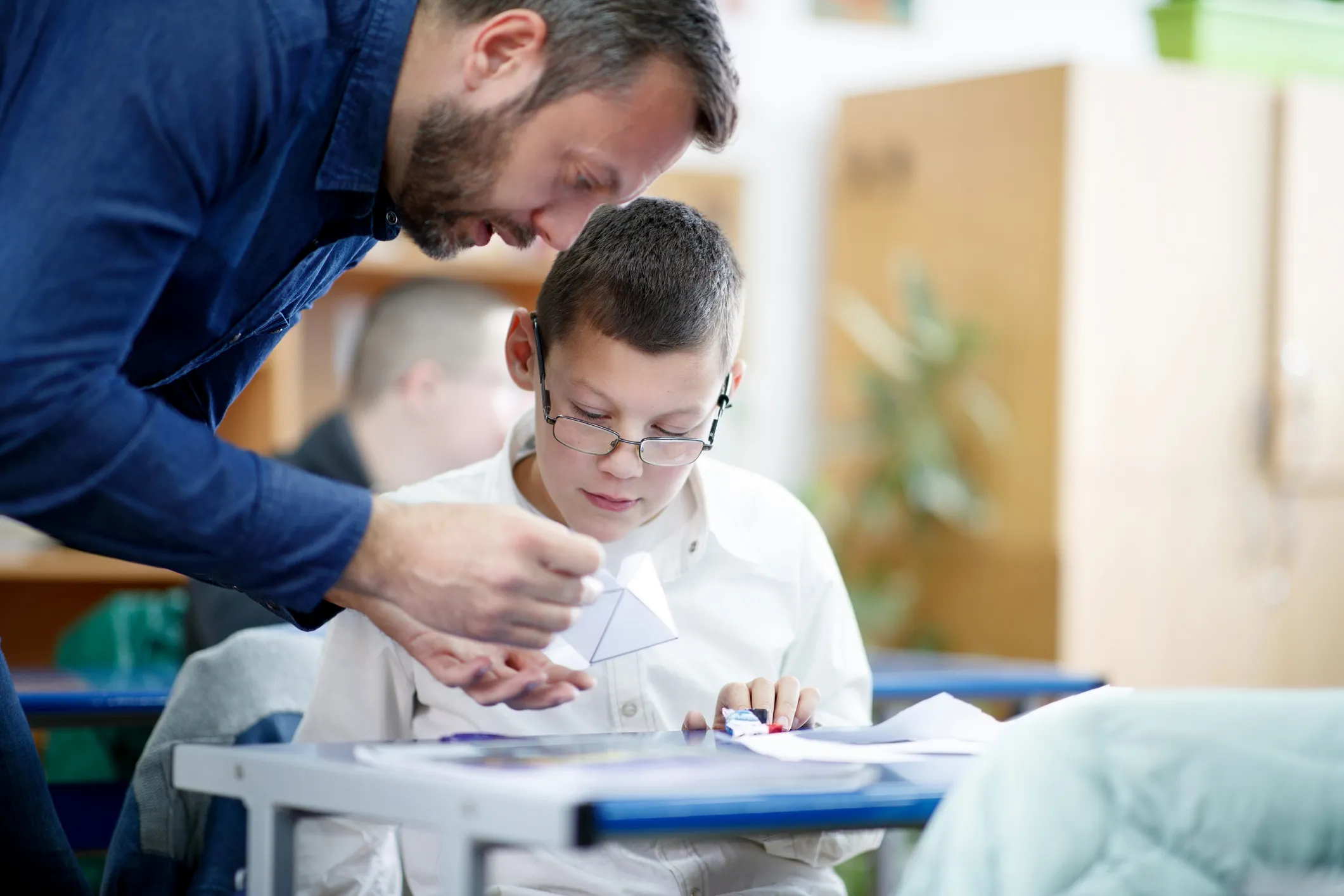 Teacher or SNA assisting a student at a classroom desk