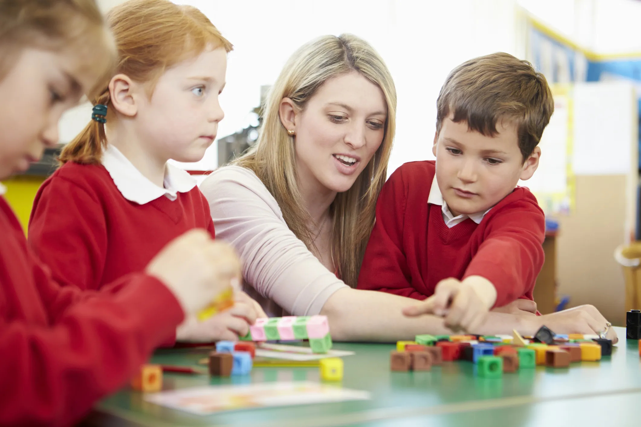 Children and a teacher working together with colourful counting blocks at a classroom table