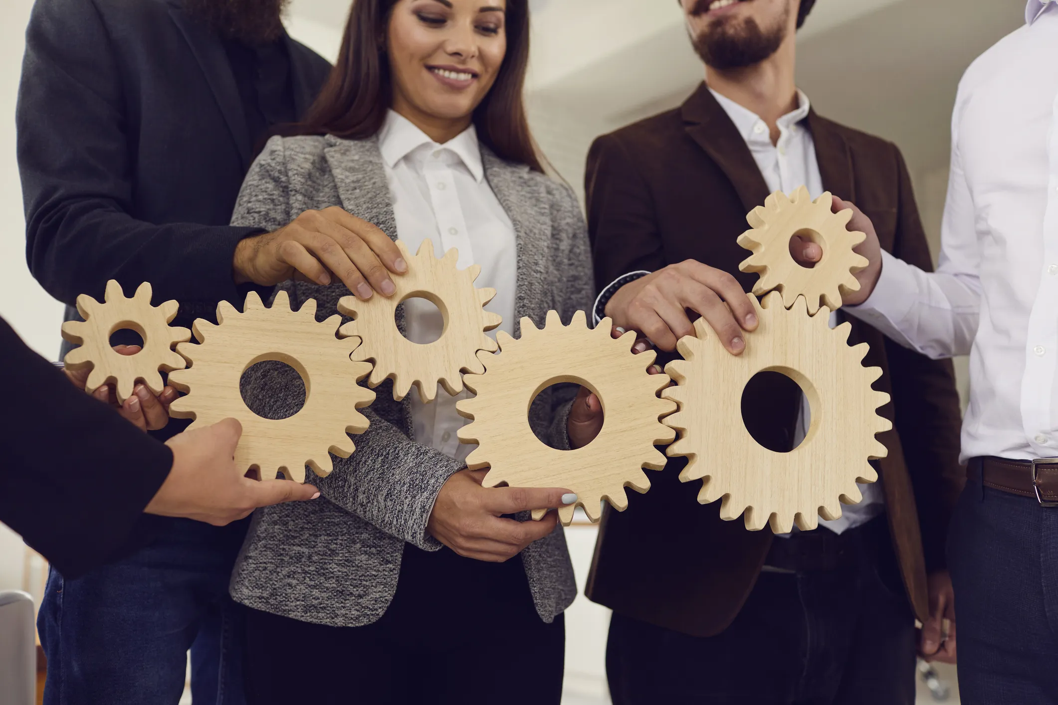 People in business attire holding interlocking wooden gears to represent teamwork