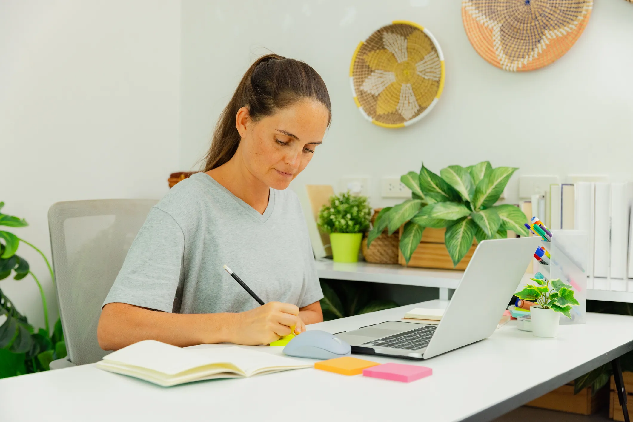 Person writing notes while working on a laptop at a desk