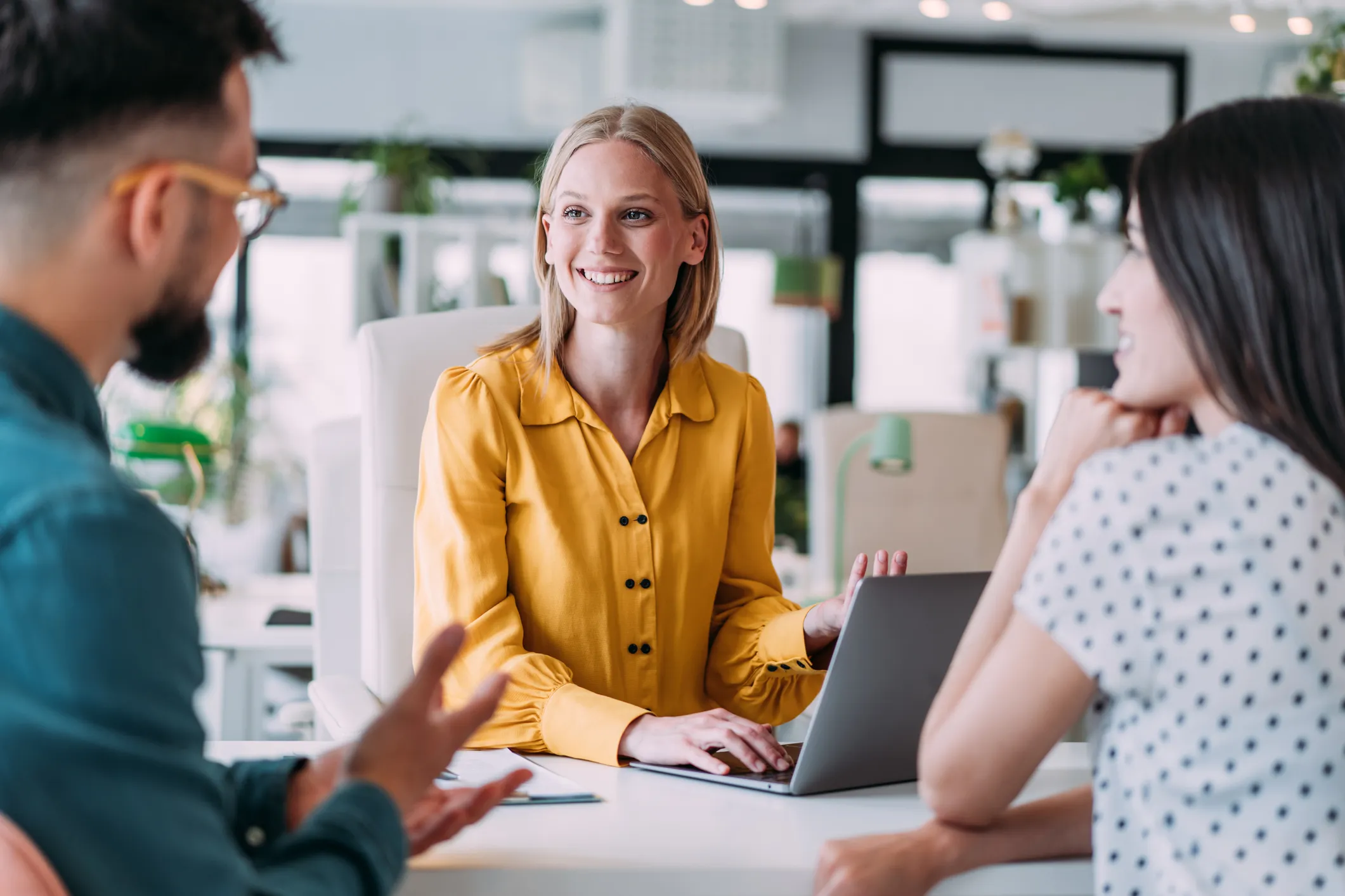 Three people having a discussion at a desk with a laptop in a office