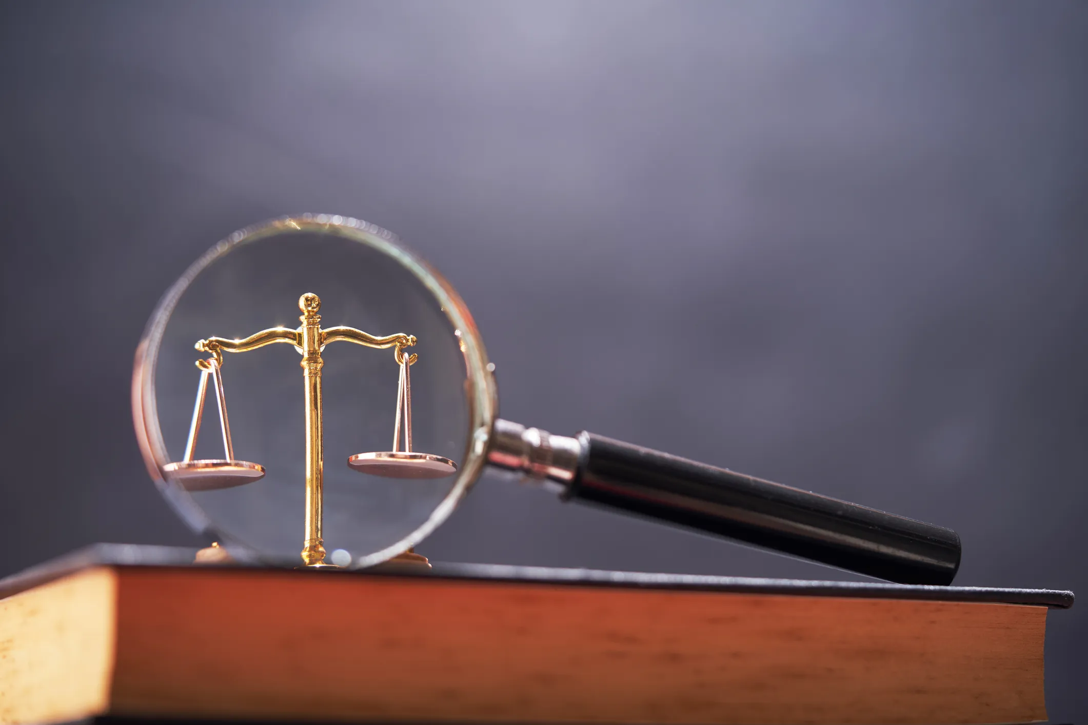 A magnifying glass focusing on a small golden justice scale