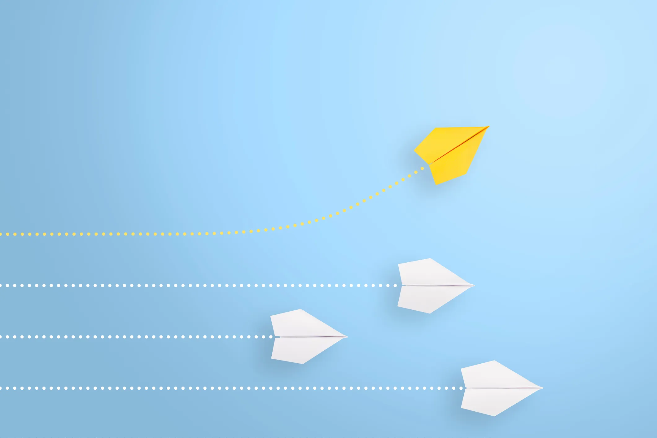 Yellow paper airplane veering upward away from three white paper airplanes