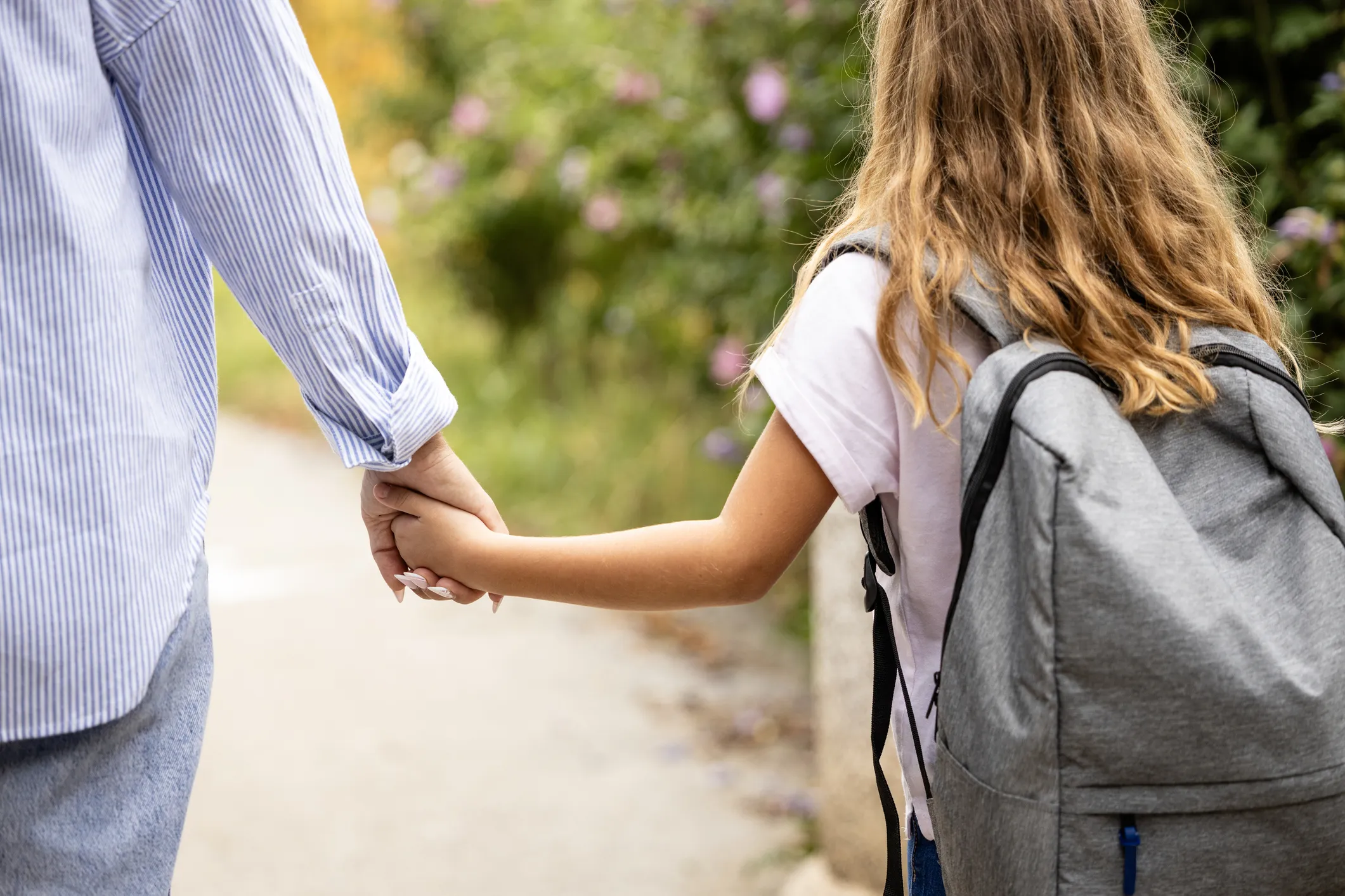 Child with backpack holding hands with an adult while walking outdoors