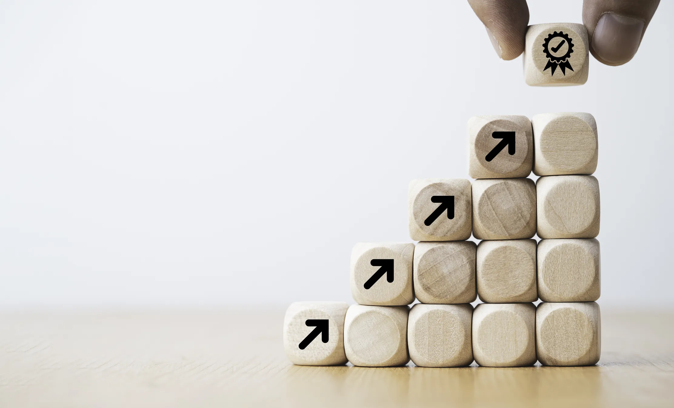 Wooden blocks stacked as steps with upward arrows, hand placing award block on top