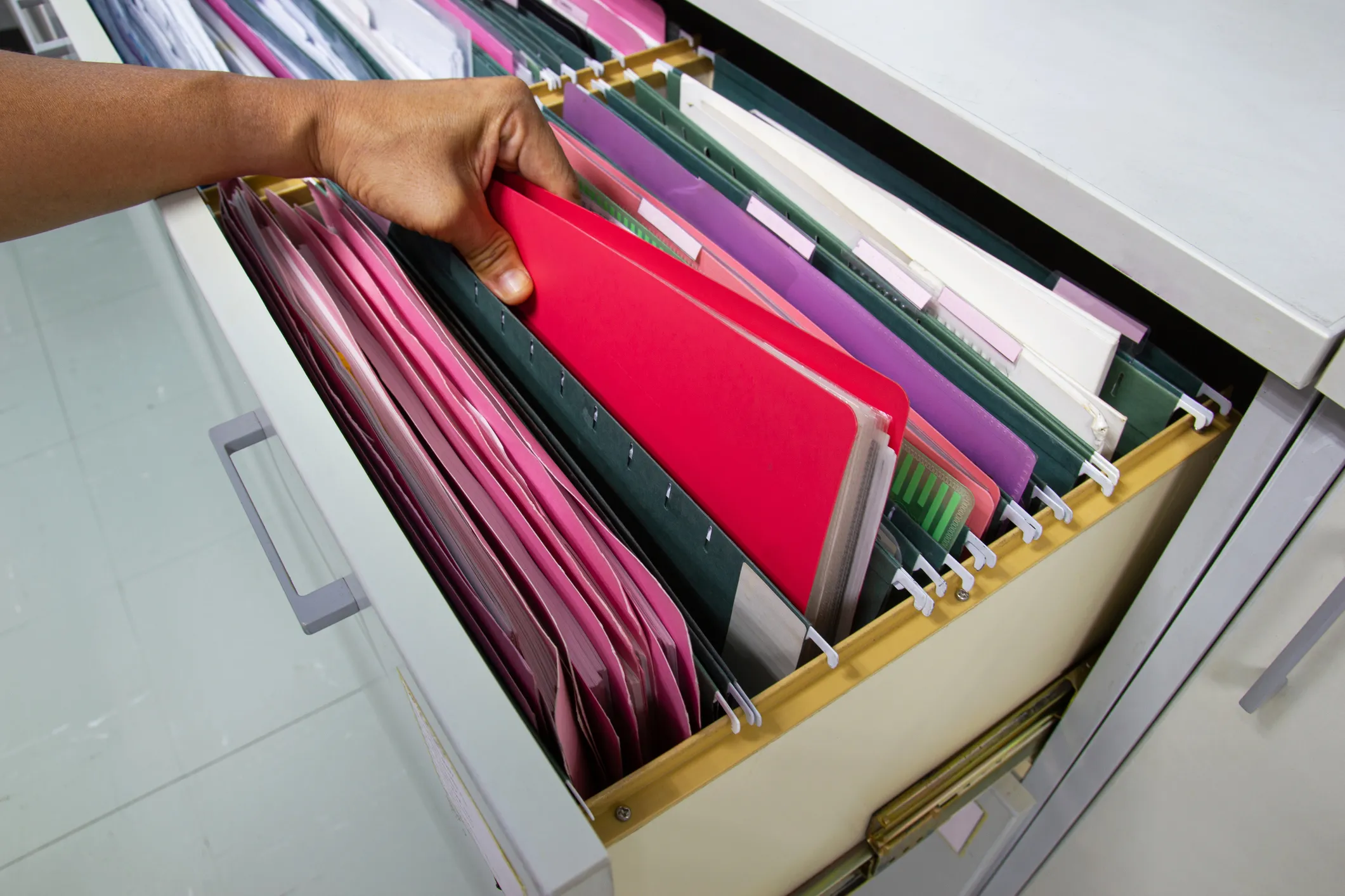 Person pulling a red folder from a filing cabinet