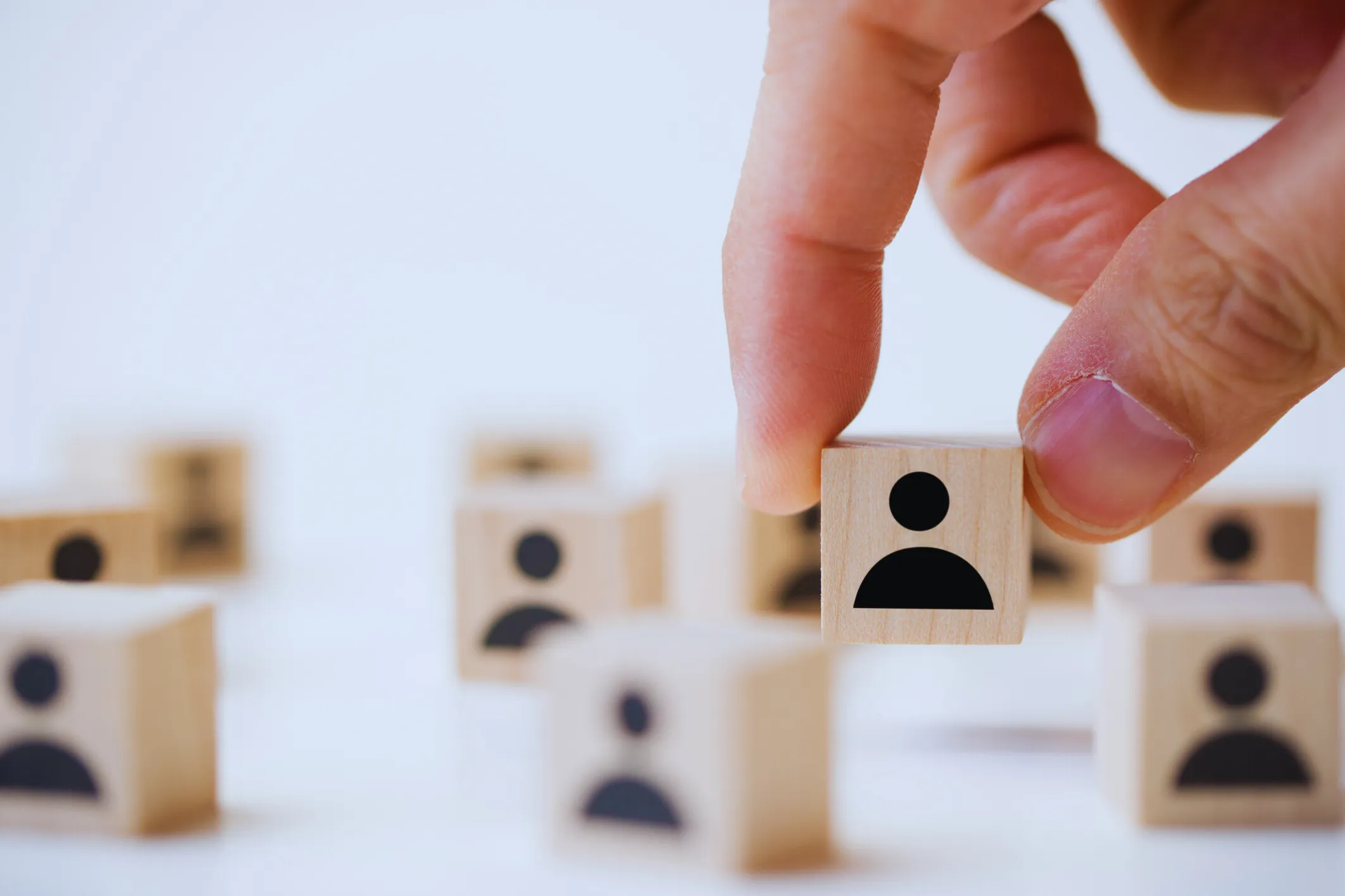 Hand picking up a wooden block with a person icon among other similar blocks symbolizing recruiting