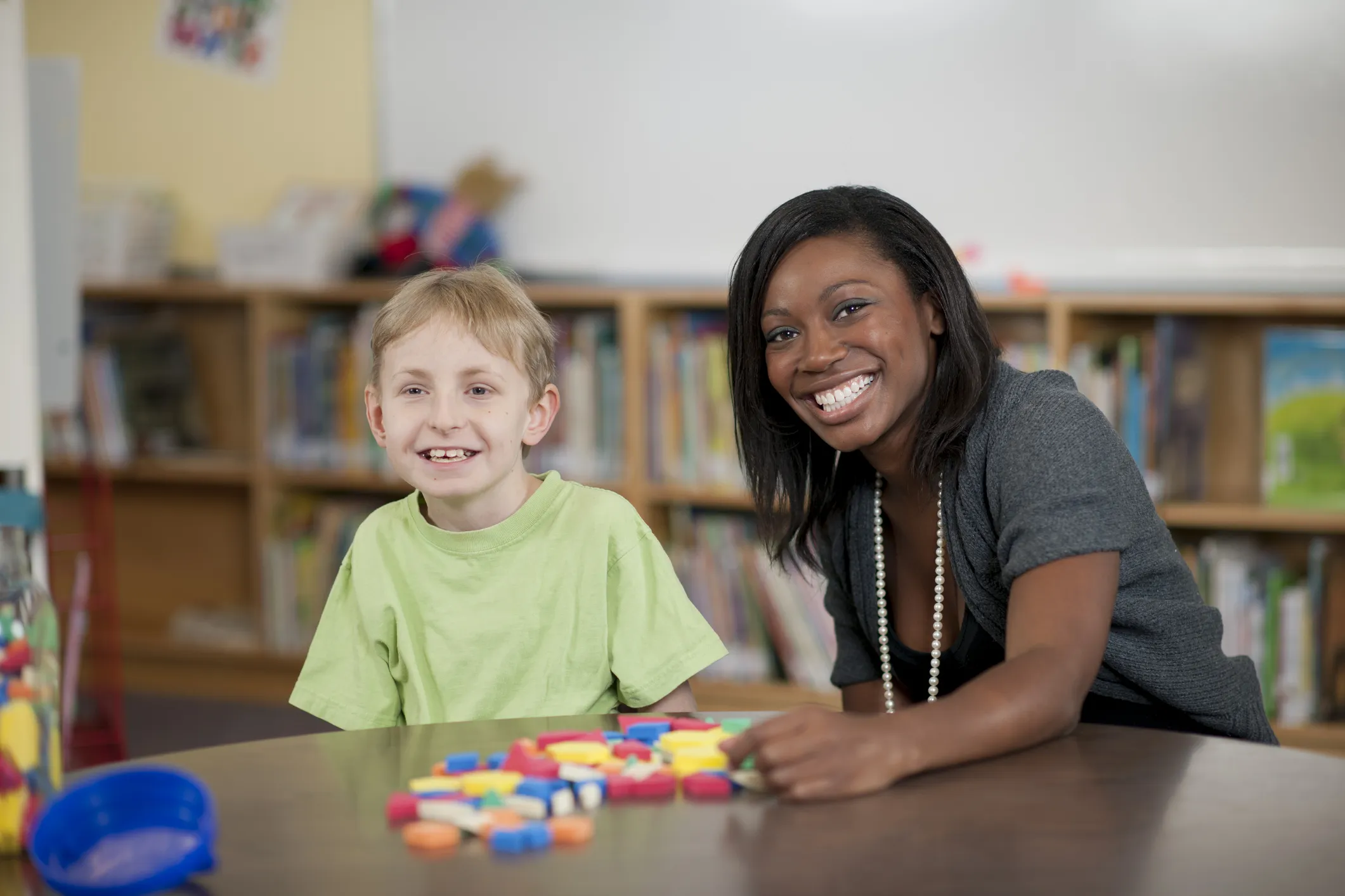 Adult and child sitting at a table with colourful learning blocks in a classroom