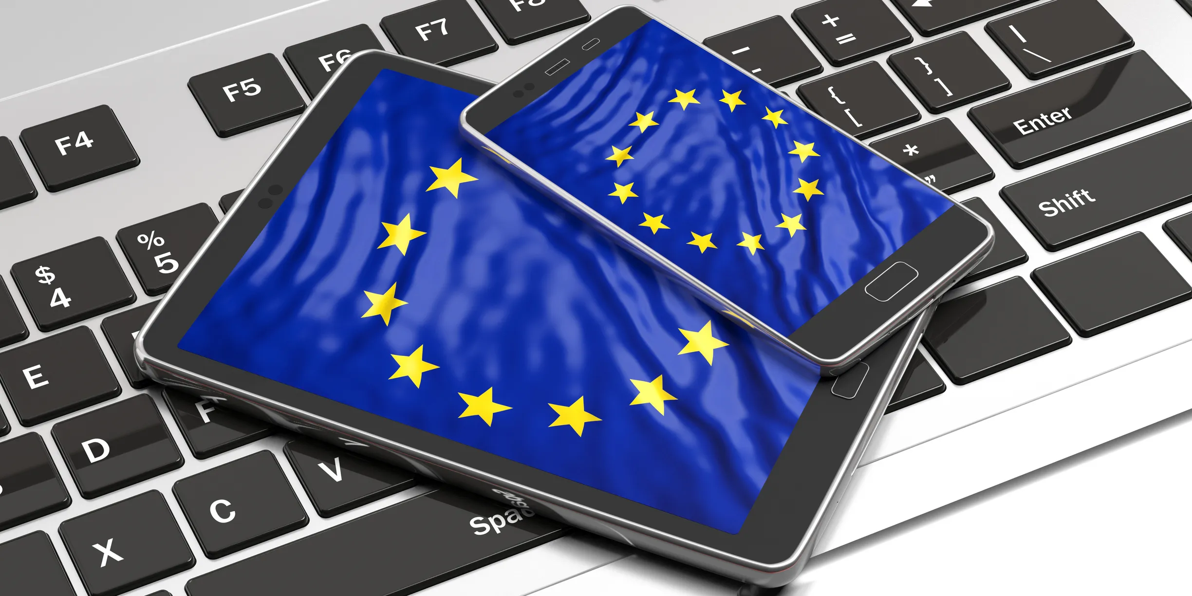 A tablet PC and mobile phone displaying the image of the European Union flag on each screen are lying on a laptop keyboard